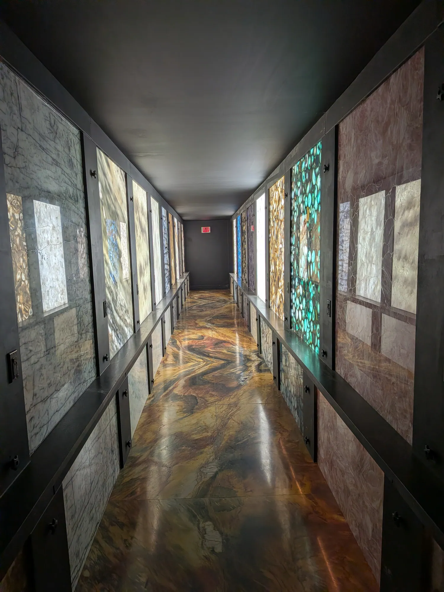 Backlit corridor with teal, pink and gray translucent panels above a glossy floor