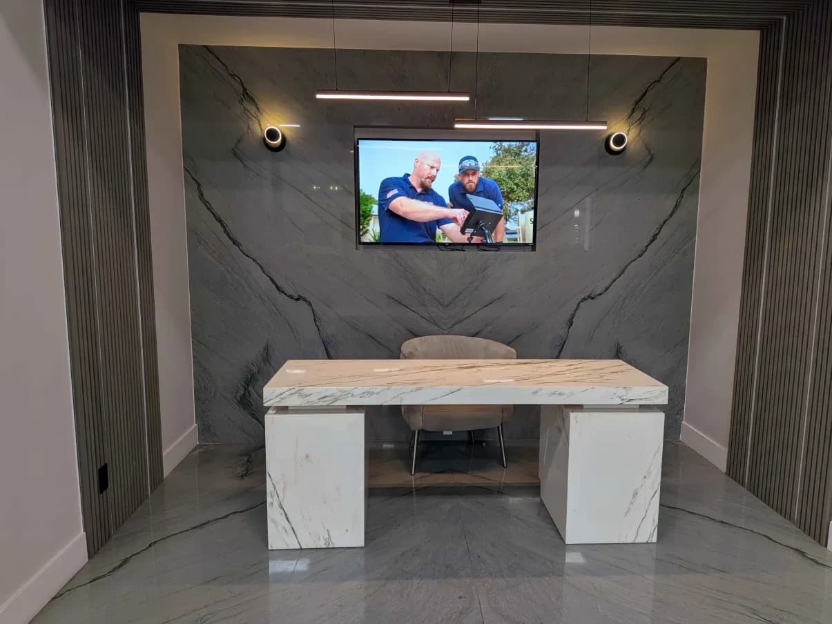 A showroom office set: a white marble waterfall desk in front of a bookmatched grey quartzite feature wall